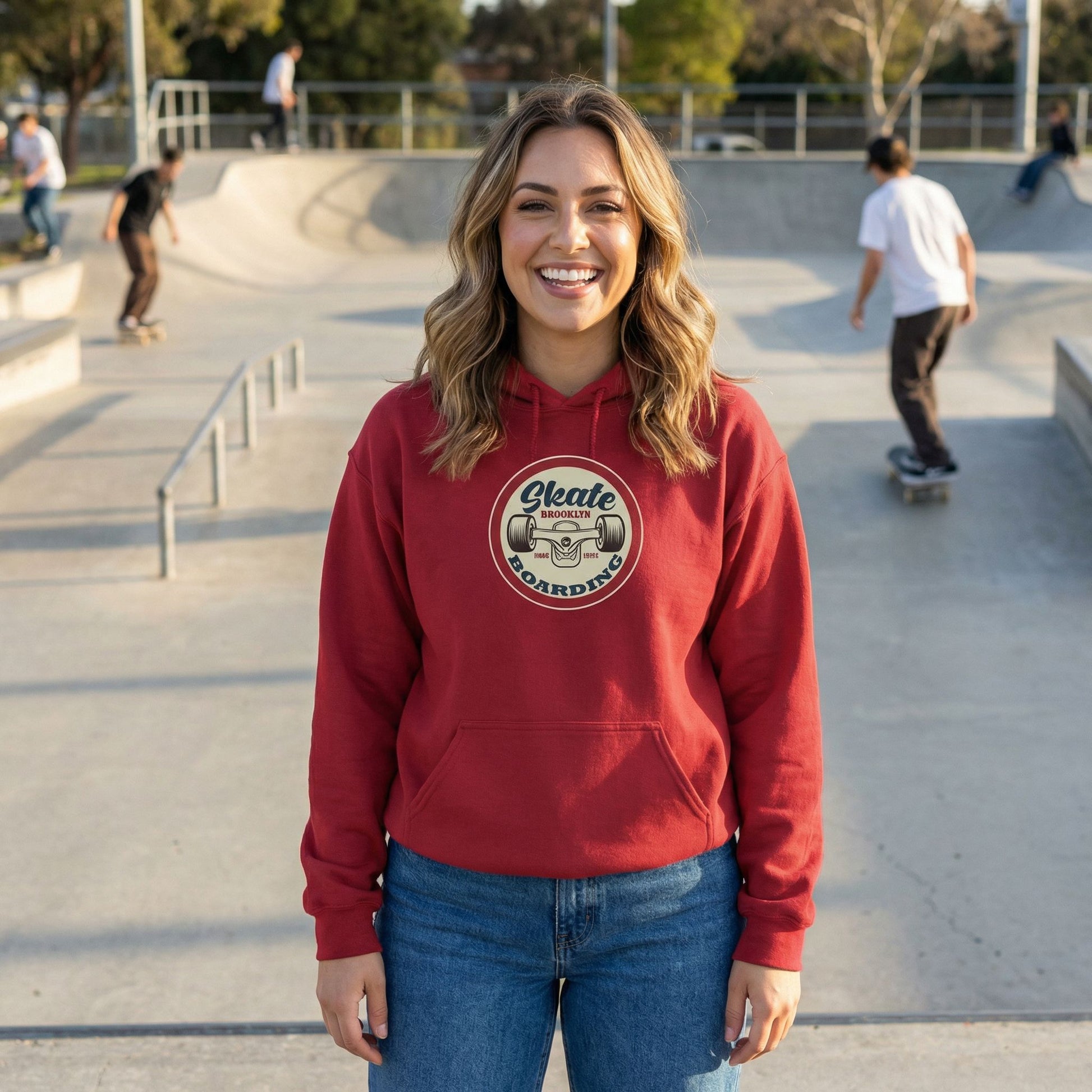 Woman wearing a red hoodie with a 'Skate Boarding' graphic at a skate park.